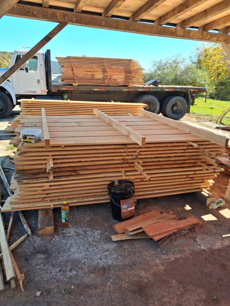 Freshly milled boards stacked under the sawmill shed roof with the white flatbed truck behind